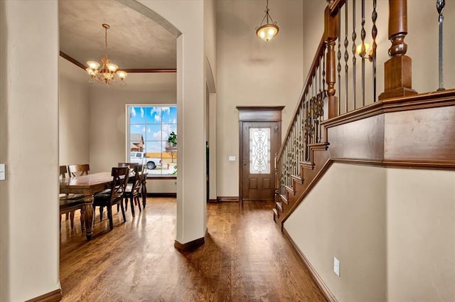 entryway featuring baseboards, stairway, ornamental molding, wood finished floors, and a chandelier