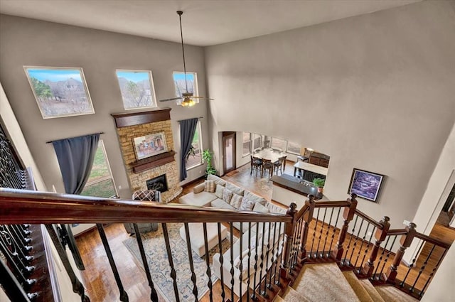 stairway featuring ceiling fan, a fireplace, a towering ceiling, and wood finished floors