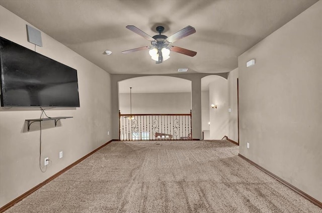 carpeted empty room with ceiling fan, arched walkways, visible vents, and baseboards