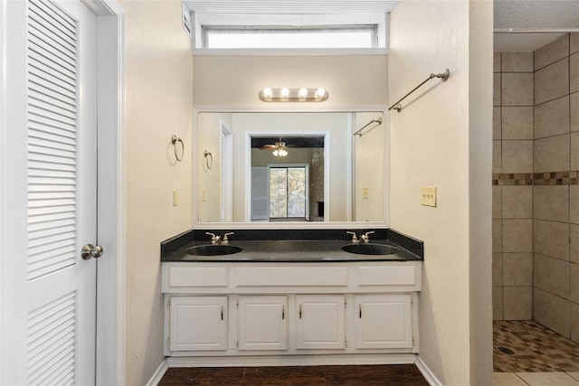 full bath with double vanity, baseboards, a tile shower, and a sink