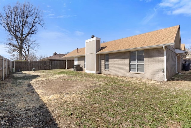 rear view of house with roof with shingles, a fenced backyard, a chimney, a lawn, and brick siding