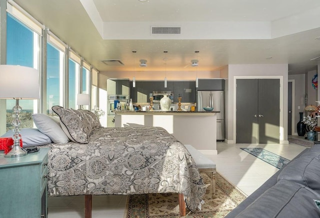 bedroom featuring a tray ceiling, visible vents, light wood-style floors, and freestanding refrigerator