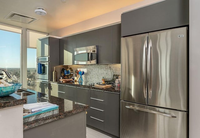 kitchen featuring visible vents, dark stone counters, a sink, stainless steel appliances, and tasteful backsplash