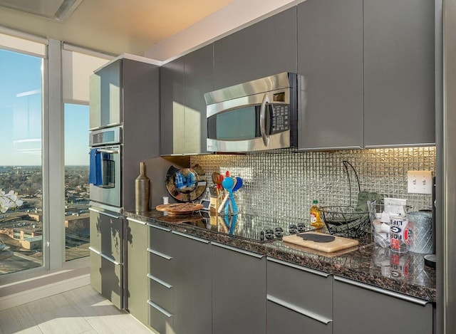 kitchen with dark stone counters, gray cabinets, stainless steel microwave, black electric stovetop, and backsplash