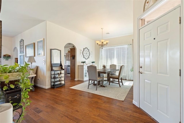 dining room with dark wood-type flooring, arched walkways, a notable chandelier, and baseboards