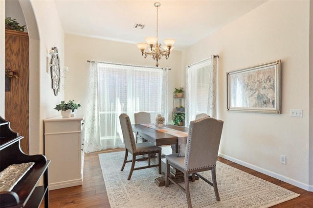 dining space featuring arched walkways, wood finished floors, visible vents, baseboards, and an inviting chandelier