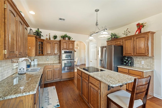 kitchen featuring arched walkways, visible vents, a center island, stainless steel appliances, and a sink