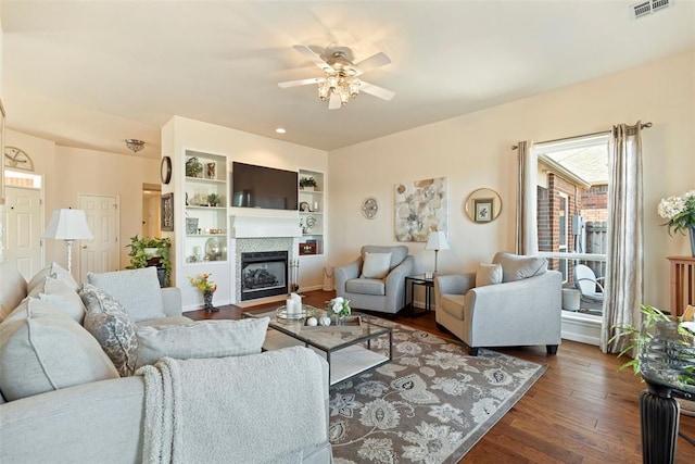 living room featuring visible vents, a fireplace with flush hearth, ceiling fan, dark wood-type flooring, and built in shelves