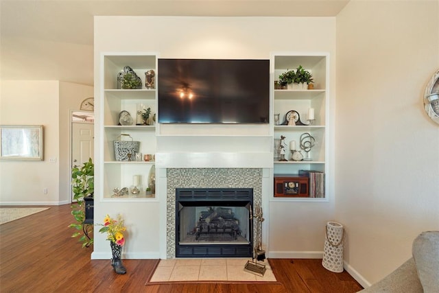 living room with baseboards, a tile fireplace, wood finished floors, and built in features