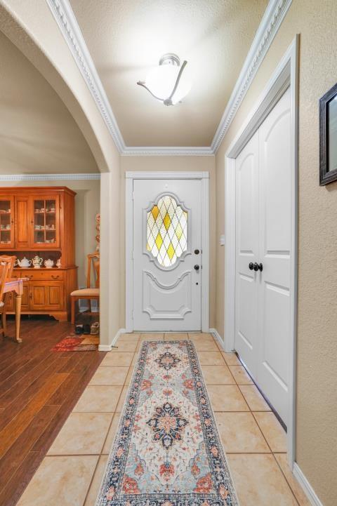 entryway with light tile patterned floors, arched walkways, and crown molding