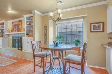 dining area with ornamental molding, a fireplace with raised hearth, a notable chandelier, and wood finished floors