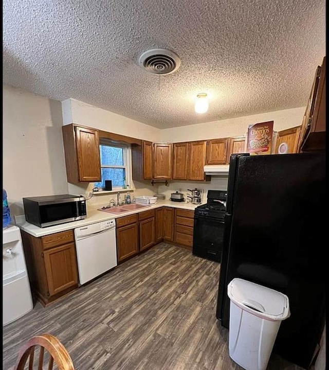 kitchen with brown cabinetry, visible vents, dark wood-style flooring, a sink, and black appliances