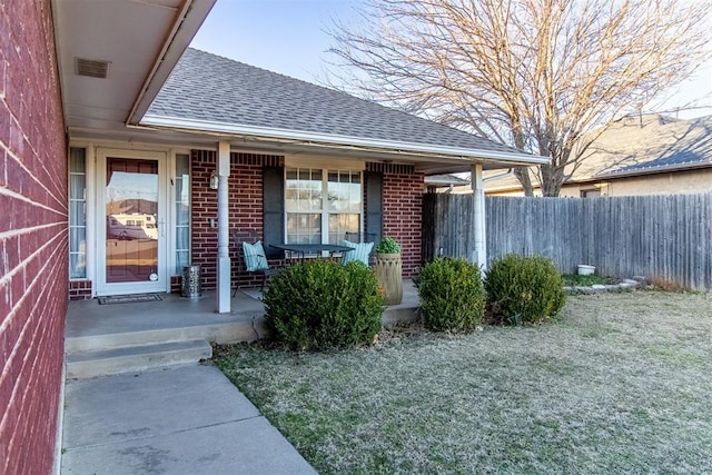 doorway to property with covered porch, a shingled roof, fence, and brick siding