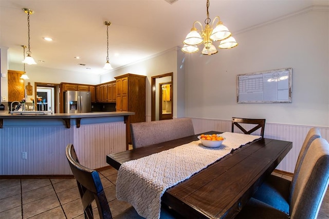 dining room with a wainscoted wall, light tile patterned floors, ornamental molding, and a chandelier