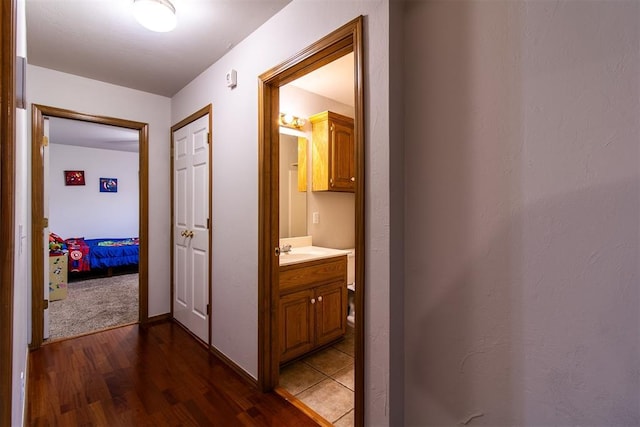 corridor featuring dark wood-type flooring, a sink, and baseboards