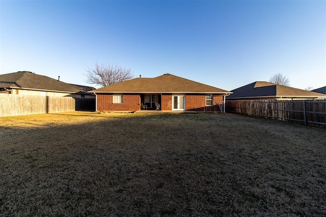 rear view of house featuring brick siding, a fenced backyard, and a yard