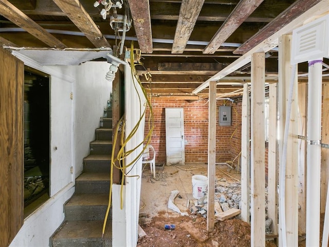 unfinished basement featuring stairway, electric panel, and brick wall