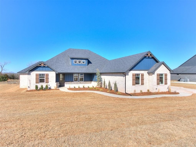 view of front of property with roof with shingles, brick siding, and a front lawn