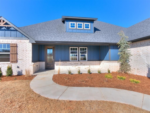 view of front of house with brick siding, roof with shingles, and board and batten siding