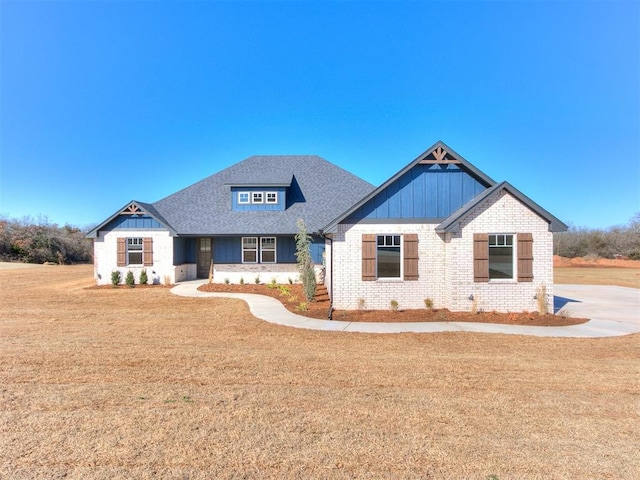 view of front facade with board and batten siding, brick siding, a front lawn, and roof with shingles