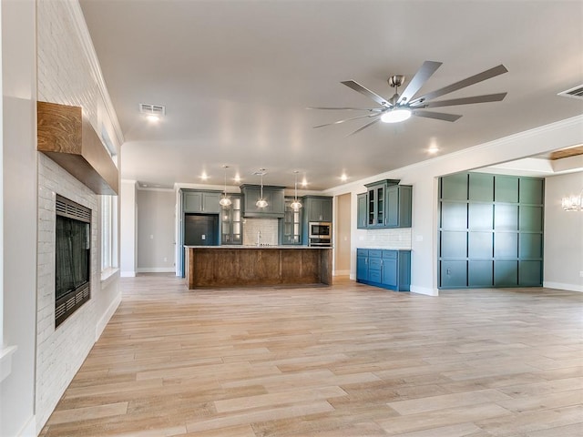 unfurnished living room featuring ornamental molding, light wood-style flooring, a brick fireplace, and visible vents