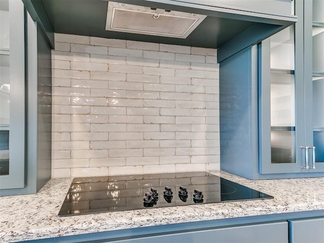 room details with glass insert cabinets, tasteful backsplash, blue cabinetry, and black electric cooktop