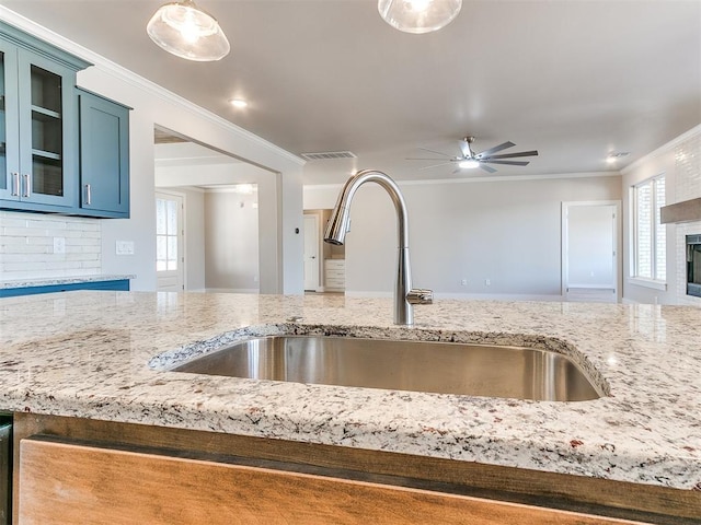 kitchen with a fireplace, a sink, visible vents, ornamental molding, and light stone countertops