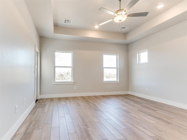 empty room featuring a raised ceiling, visible vents, light wood-style flooring, and baseboards