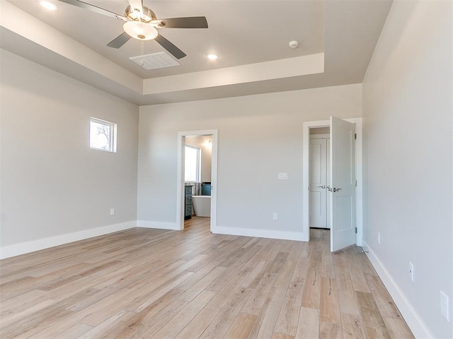 unfurnished bedroom featuring a raised ceiling, light wood-style flooring, and baseboards