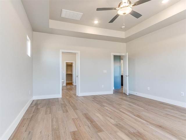 unfurnished room featuring baseboards, visible vents, a ceiling fan, a tray ceiling, and light wood-style floors