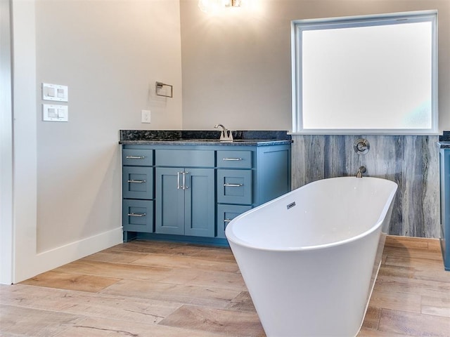 bathroom with a freestanding bath, baseboards, wood finished floors, and vanity