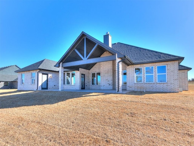 view of front of home featuring roof with shingles, a chimney, a front lawn, and brick siding