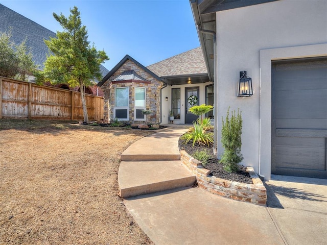 doorway to property featuring stone siding, fence, and stucco siding