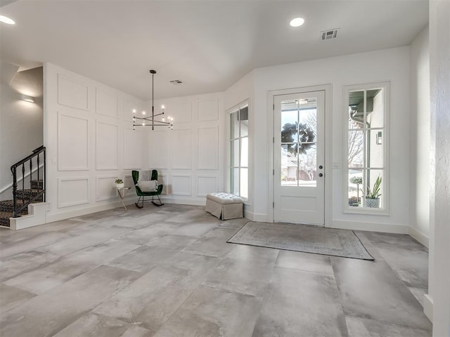 entrance foyer featuring baseboards, visible vents, stairs, a decorative wall, and a notable chandelier