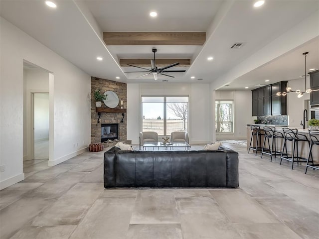 living room featuring beam ceiling, visible vents, ceiling fan, a stone fireplace, and baseboards