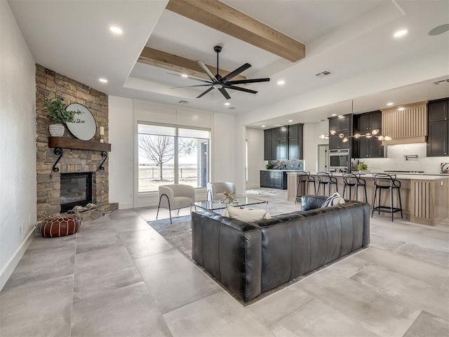 living room featuring ceiling fan, a fireplace, visible vents, baseboards, and beam ceiling