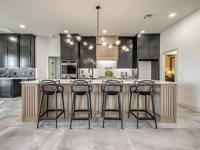 kitchen featuring oven, visible vents, light countertops, a large island, and decorative backsplash