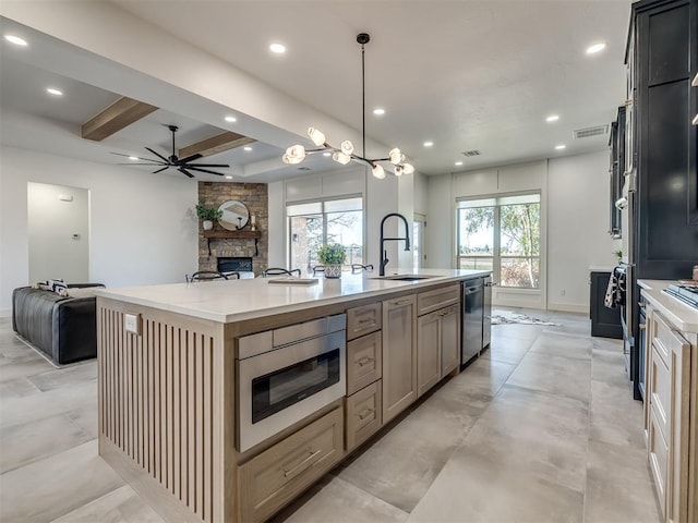 kitchen with pendant lighting, appliances with stainless steel finishes, open floor plan, a stone fireplace, and an island with sink