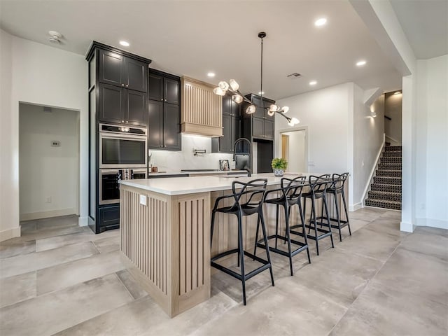 kitchen featuring recessed lighting, light countertops, decorative backsplash, double oven, and a large island with sink