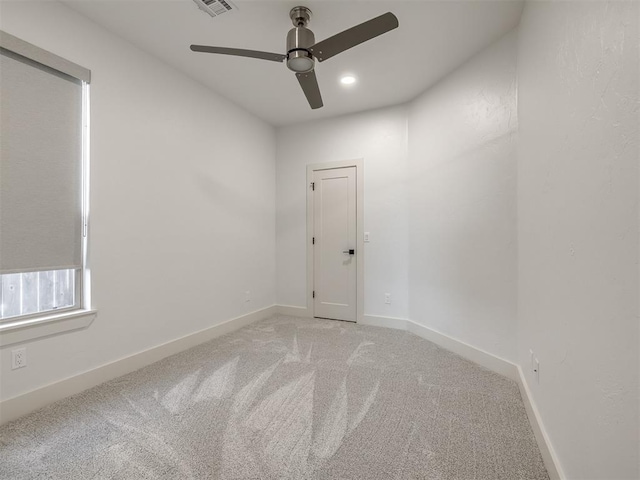 spare room featuring a ceiling fan, light colored carpet, visible vents, and baseboards