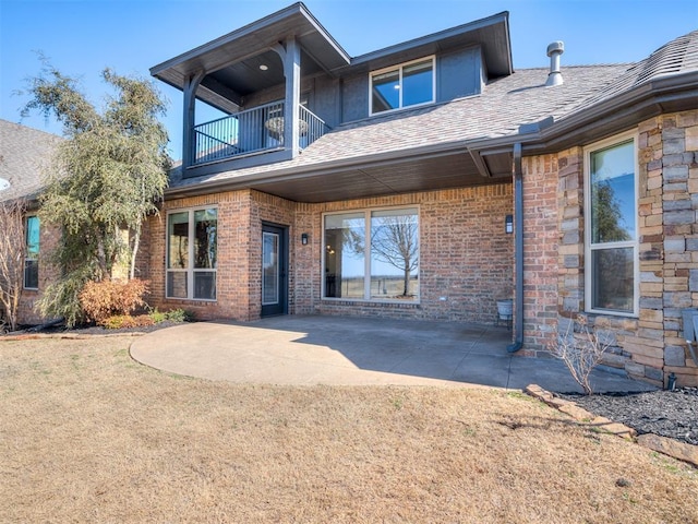 exterior space with brick siding, a shingled roof, a patio area, a balcony, and stone siding