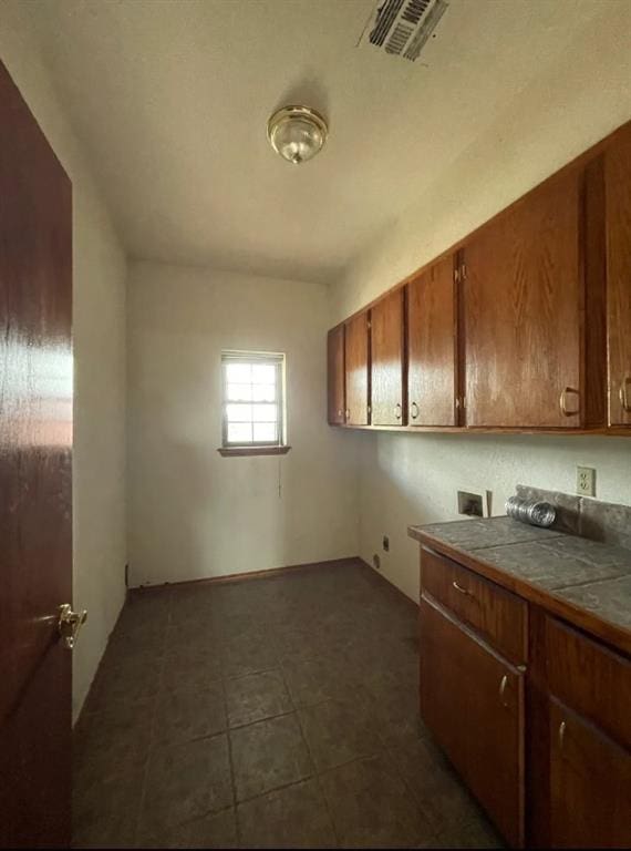 kitchen with dark tile patterned floors, visible vents, tile counters, and brown cabinetry