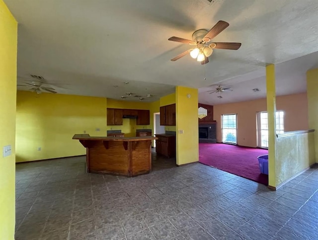 kitchen with ceiling fan, a kitchen island, open floor plan, a kitchen bar, and a fireplace