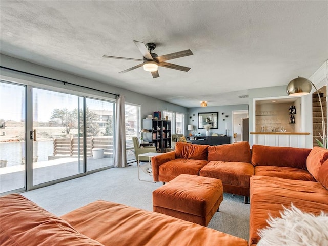 living room featuring light carpet, ceiling fan, and a textured ceiling