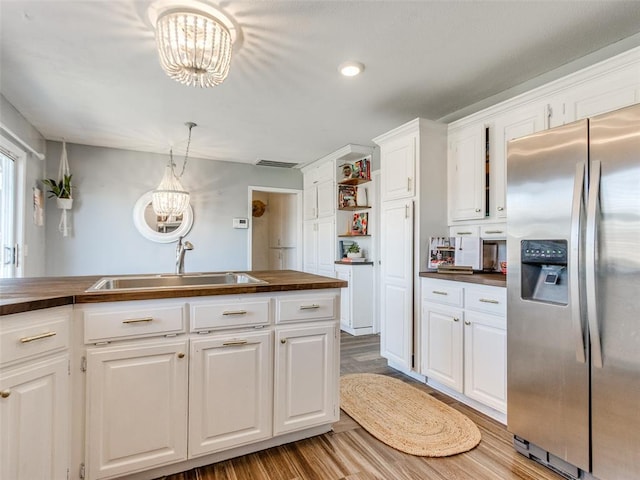 kitchen with light wood finished floors, stainless steel refrigerator with ice dispenser, white cabinetry, wooden counters, and a sink