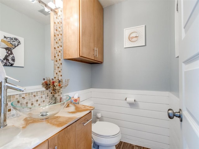 bathroom featuring a wainscoted wall, toilet, wooden walls, vanity, and wood finished floors