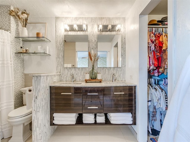 full bath with double vanity, toilet, a walk in closet, and a sink