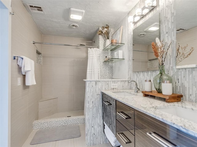 bathroom with visible vents, a sink, a tile shower, and double vanity