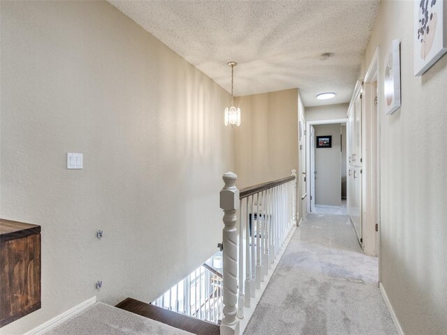 hallway featuring a textured ceiling, a textured wall, an upstairs landing, and light colored carpet