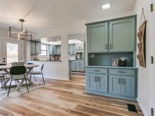 kitchen with light wood finished floors, visible vents, backsplash, stainless steel oven, and a sink